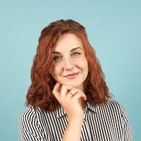 Jane Sandcastle has red shoulder-length hair and is resting a hand on her chin
